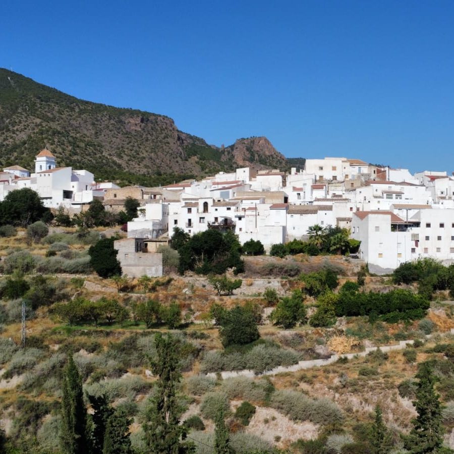 Vista de Urrácal: casas blancas en la ladera, con la sierra detrás y el cielo azul